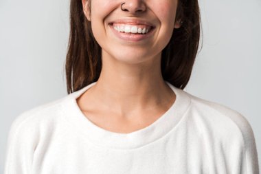 Kapalı giyinen, dişlek bir gülümsemeyle duran başarılı, güzel, stil sahibi genç bayana yakından bakın. Stüdyo çekimi beyaz arkaplanda izole edildi