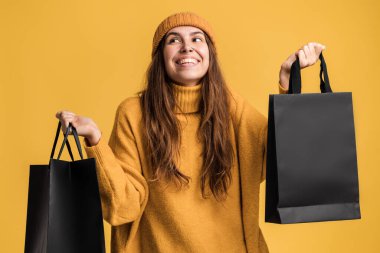 Alışveriş torbalarını kaldıran, paketlerle harika hisseden ve düşük fiyatları kutlayan aşırı hevesli bir kadının portresi. Kara Cuma konsepti. Moda mağazasının reklamı. 