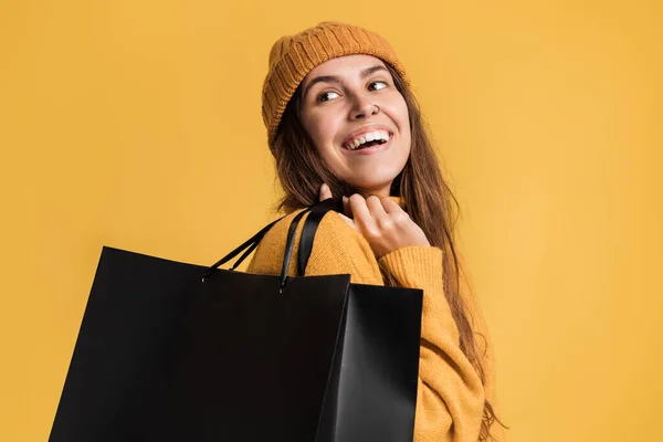 一个快乐的女人穿着休闲装 提着购物袋 隔着黄墙背景望向远方的画像 — 图库照片