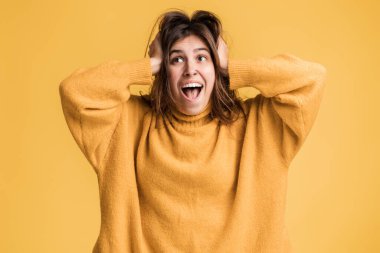 Vay canına. Uzun saçlı, şapkalı mutlu genç bir kadının portresi çığlık atıyor ve zaferini şaşkın bir heyecanla kutluyor. Sarı arka planda kapalı stüdyo çekimleri 