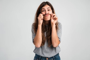 Saçları esmer, sevimli komik kızın belden aşağısı portre görüntüsü. Saçma sapan komik suratlar yapıyor ve saçlarıyla oynuyor. Beyaz arka planda izole edilmiş kapalı stüdyo görüntüleri 