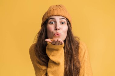 Öpücüğümü yakala. Güzel romantik esmer kız kameraya bakıyor avuçların üzerinden öpüşüyor, sevgilerini gönderiyor. Güzellik ve moda modası. Sarı arka planda kapalı stüdyo çekimleri 