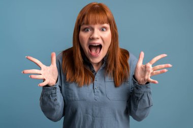Wow, I can't believe this. Portrait of astonished woman with widely open mouth in amazement and big eyes looking at camera, stunned shocked face. Indoor studio shot isolated on blue background 