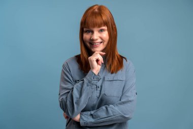 Portrait view of calm beautiful young woman standing with happy face, expressing positive. Indoor studio shot isolated on blue background 
