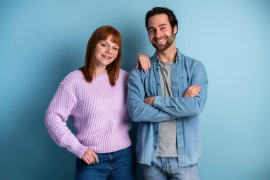 Portrait of cheerful young caucasian couple standing together and bonding to each other isolated over blue background. People concept 