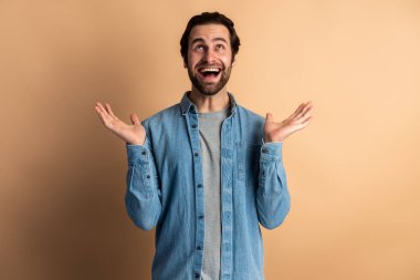 Excited shocked man holding hands near face and screaming looking up with big eyes and open mouth, shocked bemused with news, win at lottery. Indoor studio shot isolated on orange background 