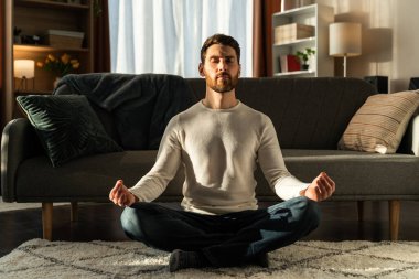 Caucasian man meditating in lotus pose and with closed eyes at home. Sport, fitness and healthy lifestyle concept 