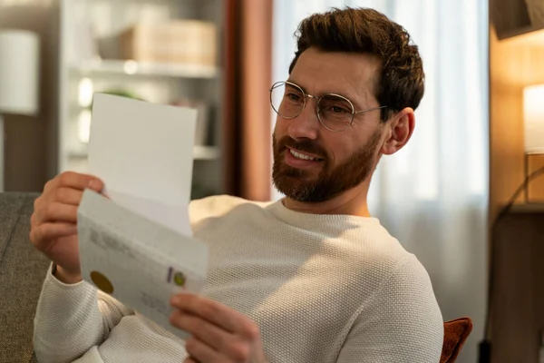 Millennial guy wearing glasses reading pleasant news in postal letter. Happy young man considering paperwork and getting good answer in post correspondence. 