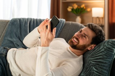 Portrait view of the young caucasian man messaging on smartphone at home with toothy smile. People and technologies concept 