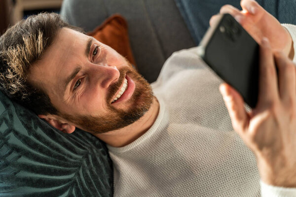 Portrait view of the young caucasian man messaging on smartphone at home with toothy smile. People and technologies concept 