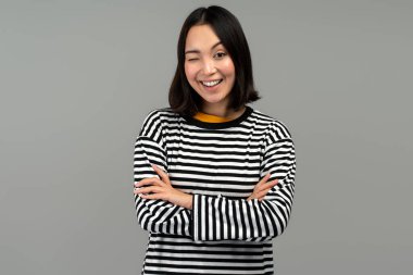 Pozitif kadın kameraya göz kırpıyor, flört ediyor, kurnaz bir fikri olduğu için göz kırpıyor. Kapalı alanda çekilen çekim gri arka planda izole edildi