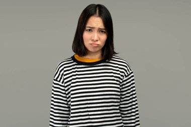 Mutsuz bir kadın kameraya somurtkan dudaklarıyla bakıyor, kötü haberlere üzülüyor. Kapalı alanda çekilen çekim gri arka planda izole edildi