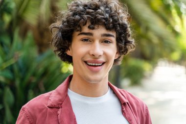 Yeşil Park 'ta yürüyen genç adamın portre görüntüsü. Kameraya gülümseyen kendinden emin adam. Yaşam tarzı kavramı 