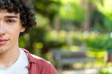 Dışarıdaki kameraya bakan mutlu adamın yarım portresi. Kıvırcık adam gün batımında mutlu ve kendinden emin hissediyor. Arka planda ağaçlarla gülümseyen çocuğun yakın yüzü 