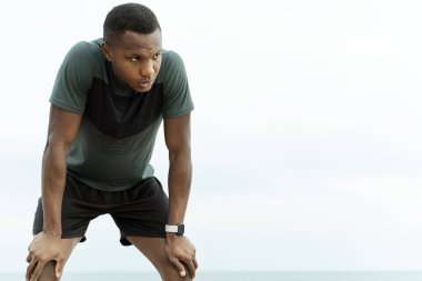 Yorgun ve çok ırklı koşucunun portresi sıkı bir eğitimden sonra deniz kenarında dinlenirken. Spor ve eğlence konsepti