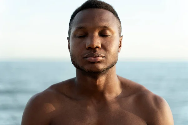 Portrait of the handsome fitness multiracial man at the beach on a sunny day standing with closed eyes and relaxing. Stock photo