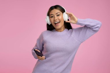 Kulaklıklı mutlu çılgın kadın pembe renkte neşeli bir şekilde şarkı söylüyor. Menekşe kazaklı neşeli kadın gülüyor ve şarkı söylüyor. 