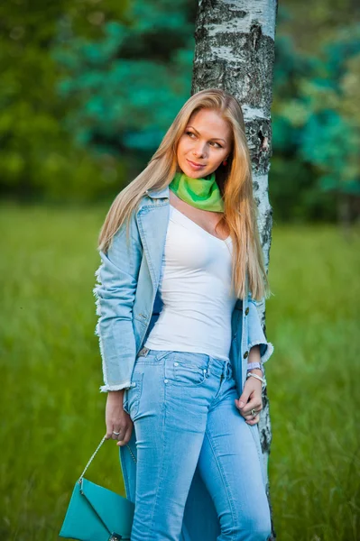 Очень привлекательная молодая девушка, позирующая в джинсах и синем пальто на открытом воздухе летом. — стоковое фото