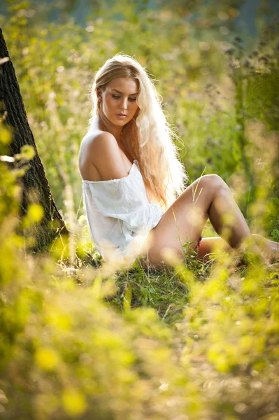 年轻漂亮的金发姑娘穿着白色衣服坐在草 — 图库照片