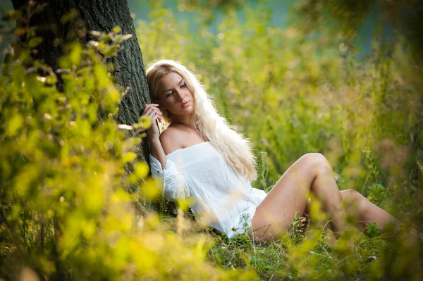 Pretty young blonde girl in white dress sitting in grass — Stock Photo, Image