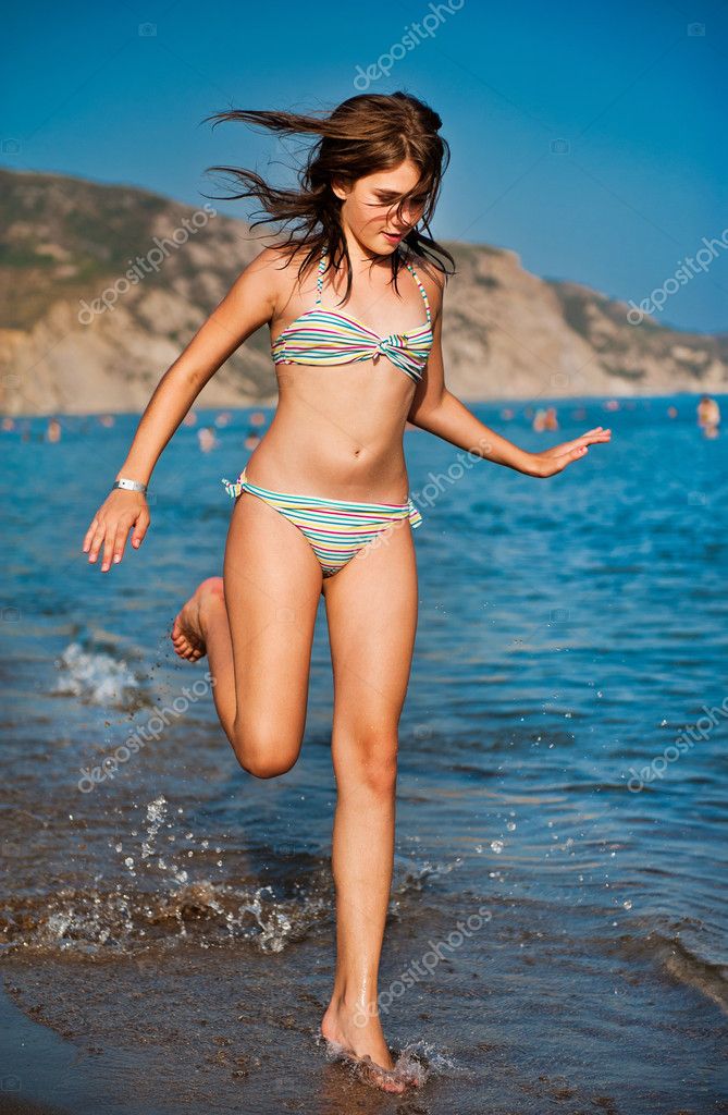 Attractive slim teenager girl in bikini runs along the beach Stock