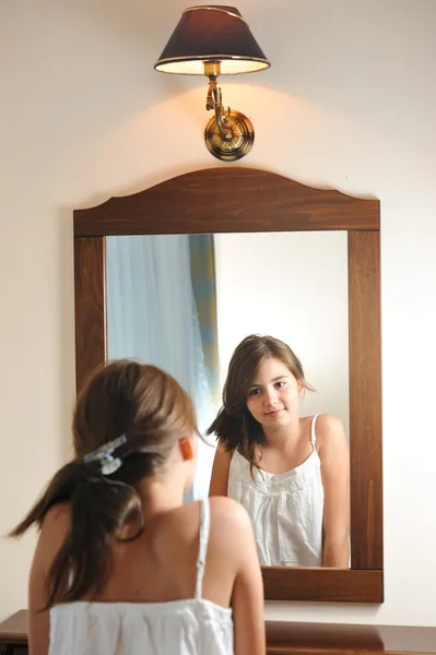 Uma linda menina adolescente estuda sua aparência enquanto olha para o espelho em sua bela reflexão jovem. Menina adolescente feliz com sua aparência no espelho — Fotografia de Stock