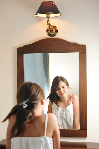 A beautiful teen girl studies her appearance as she looks into the mirror at her beautiful young reflection. Teen girl happy with their appearance in the mirror Stock Picture