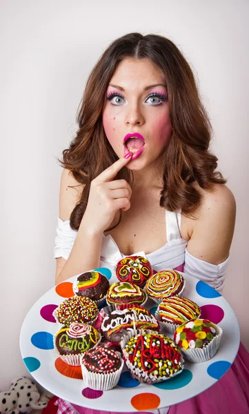 Portrait of young surprised woman eating cakes isolated on white background . Big plate with many cakes — Stock Photo, Image