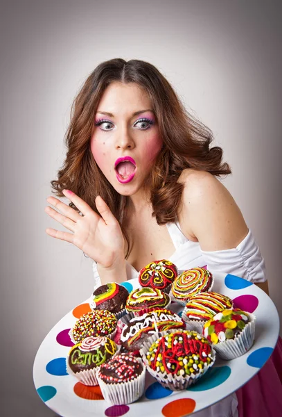 Portrait of young surprised woman eating cakes isolated on white background . Big plate with many cakes — Stock Photo, Image