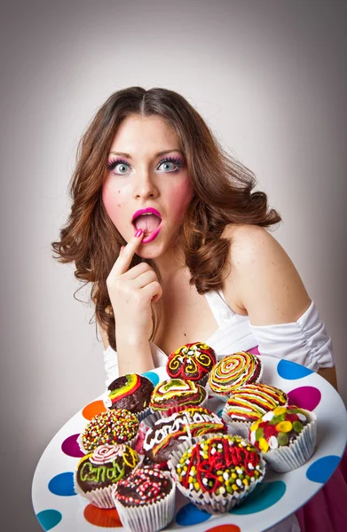 Retrato de una joven sorprendida comiendo pasteles aislados sobre fondo blanco. Placa grande con muchos pasteles — Foto de Stock