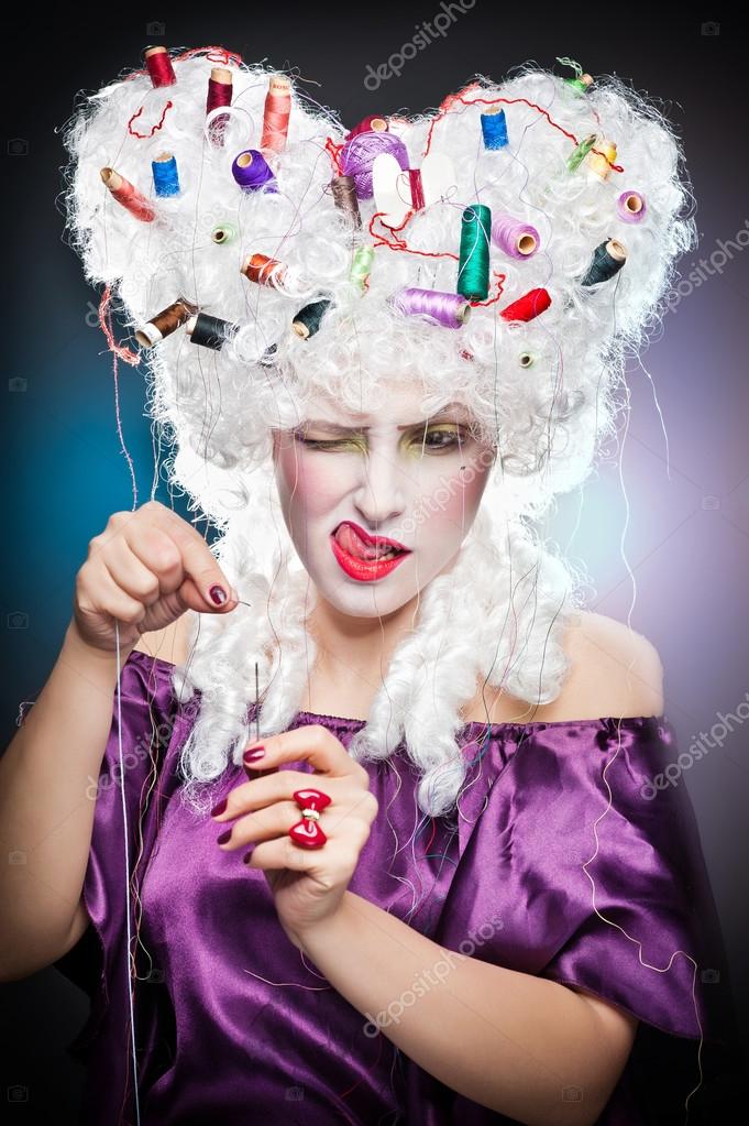 Lady focused with accessories for needlework in her wig.Vintage scene of beautiful lady with spool colored in the wig .girl with sewing accessories in her hair trying to thread a needle stick