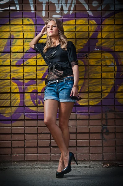 Chica de belleza posando moda cerca de la pared de ladrillo rojo en la calle. Mujer joven con gafas de sol contra una pared de graffiti —  Fotos de Stock