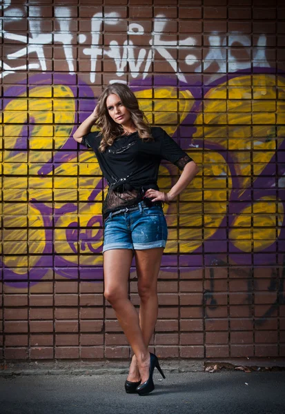 Schoonheid meisje poseren mode in de buurt van rode bakstenen muur op de straat .young vrouw met zonnebril tegen een muur met graffiti — Stockfoto