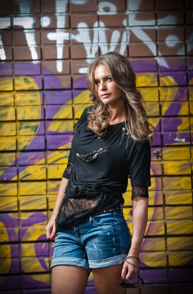 Beauty girl posing fashion near red brick wall on the street .Young woman with sun glasses against a graffiti wall — Stock Photo, Image