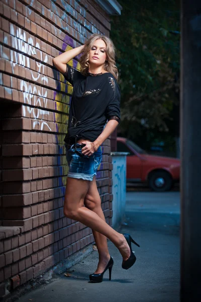 Skönhet flicka poserar mode nära röda tegelväggen på gatan .young kvinnan med solglasögon mot en graffiti vägg — Stockfoto