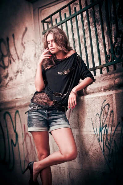 Menina de beleza posando moda perto de parede de tijolo vermelho na rua. Mulher jovem com óculos de sol contra uma parede de grafite — Fotografia de Stock