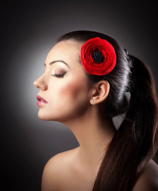 Fashion Brunette Girl with Flower isolated on textured background.Profile of makeup woman with red flower in hair on textured background.Young beautiful girl with red flower in hair posing in studio. clipart