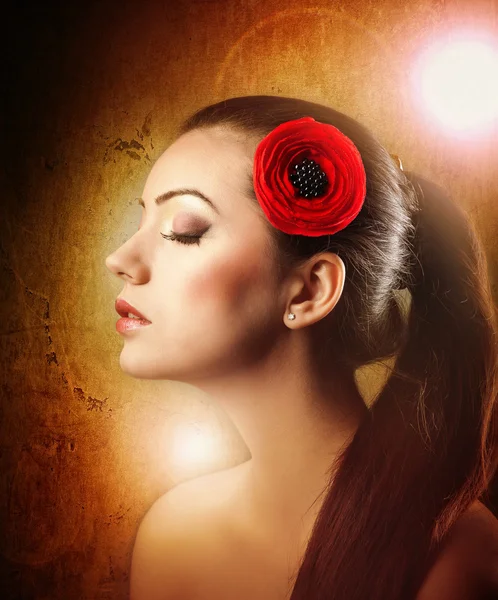 Fashion Brunette Ragazza con fiore isolato su sfondo strutturato.Profilo di donna trucco con fiore rosso in capelli su sfondo strutturato.Giovane bella ragazza con fiore rosso in capelli in posa in studio . — Foto Stock