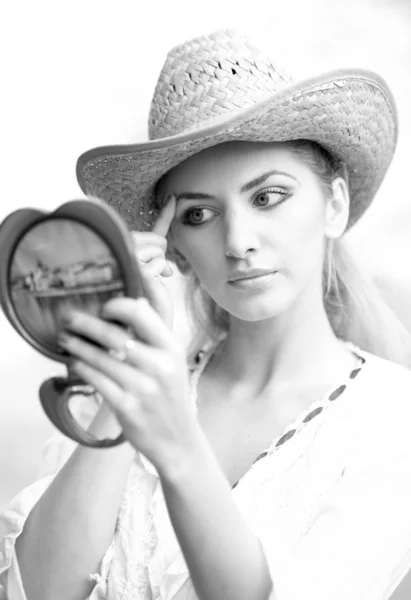 Hermosa mujer con sombrero de paja y espejo. Mujer joven mirando en espejo cosmético. Mujer hermosa de buen aspecto haciendo maquillaje delante del espejo . — Foto de Stock