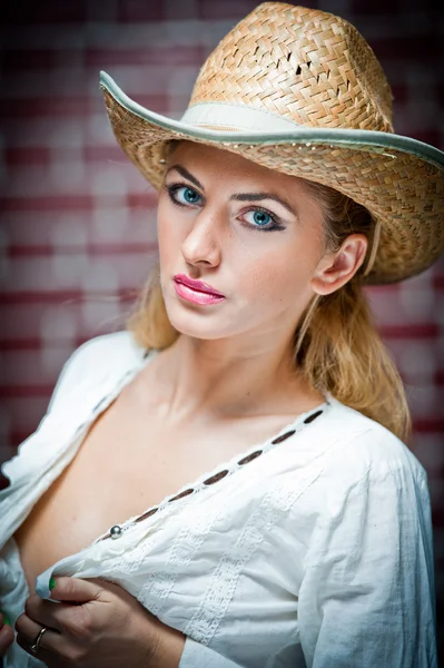 Attraente ragazza bionda con cappello di paglia e blouse.Beautiful bianco giovane donna con cappello di paglia e kaftan bianco contro un muro di mattone.Splendidi occhi biondi blu capelli mentre indossa un cappello di paglia cowboy . — Foto Stock