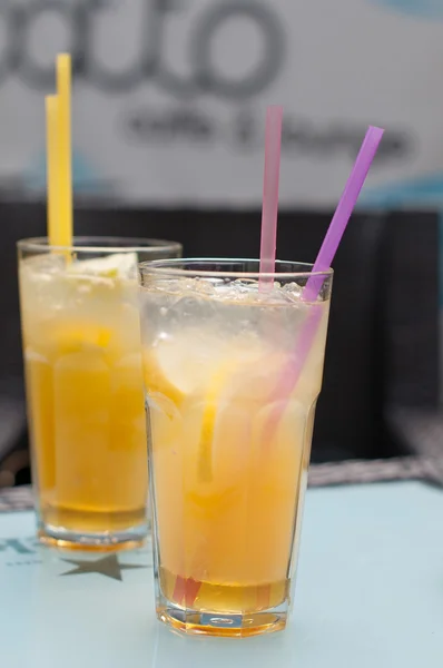 Dois copos com suco de laranja fresco com palhas e cubos de gelo em uma mesa — Fotografia de Stock