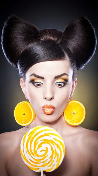 Girl with lollipop and orange slices as earrings.Creative earrings made of oranges and smile.Portrait of a woman with orange and oranges as a accessories.Portrait of beautiful woman licking lollipop — Stock Photo, Image