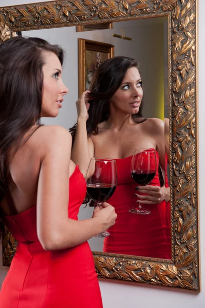 La hermosa chica en un vestido largo rojo posando en una escena vintage. Joven hermosa mujer con un vestido rojo en el viejo hotel. Jovencita elegante ensual en vestido rojo mirando en el espejo —  Fotos de Stock