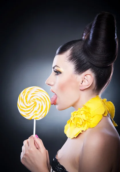 Chica de moda con piruleta amarilla y sonrisa sobre un fondo. Retrato de mujer hermosa con lollipop lamiendo pelo de belleza — Foto de Stock