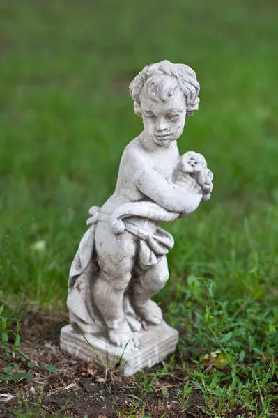 Oud standbeeld van kind en gras achtergrond .statue van een kind engel in gebed gemaakt van witte steen — Stockfoto