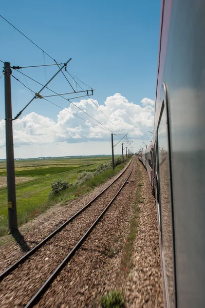 Spoorlijn gaat naar horizont in groene en gele landschap onder blauwe hemel met witte clouds.railway onder bewolkt sky.scenic spoorweg in landelijk gebied in de zomer en blauwe hemel met witte wolken. — Stockfoto