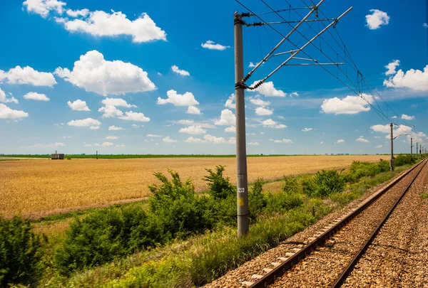 Ferrovia va all'orizzonte nel paesaggio verde e giallo sotto cielo blu con nuvole bianche.Ferrovia sotto cielo nuvoloso.Ferrovia panoramica in zona rurale in estate e cielo blu con nuvole bianche . — Foto Stock