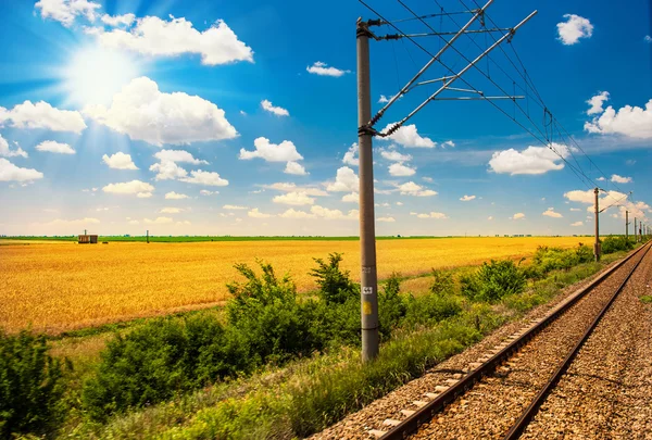 Железная дорога идет к горизонту в зеленом и желтом ландшафте под голубым небом с белыми облаками. Железная дорога в сельской местности летом и голубое небо с белыми облаками . — стоковое фото