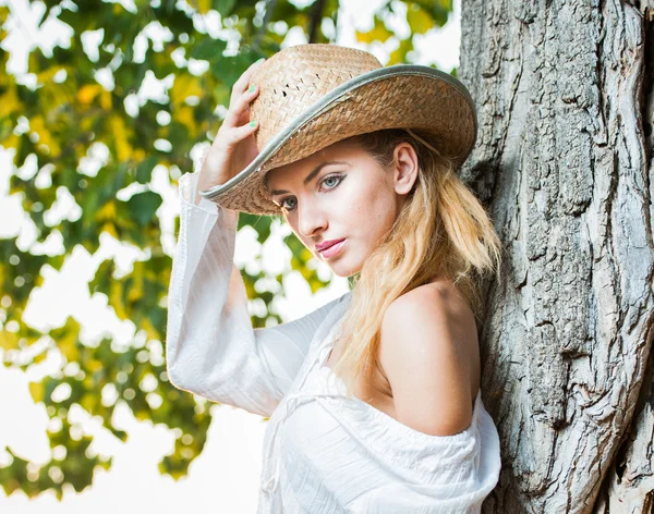 Modeporträt Frau mit Hut und weißem Hemd sitzt auf einem Heustapel.Sehr nette blonde Frau sitzt draußen auf dem gelben Gras mit Hut — Stockfoto