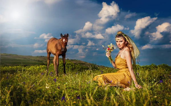 白い雲と青い空を背景の芝生のフィールド上の女性のベリー ダンサー リラックス。セクシーなアラビア トルコ東洋プロの芸術家屋外黄色の衣装とダイヤモンドのジュエリー。エキゾチックなベリーダンス スター. — ストック写真